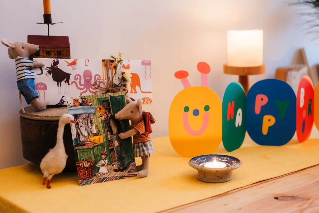 Birthday display with toy mice, a goose figure, colorful cards spelling “Happy Birthday,” and a lit candle